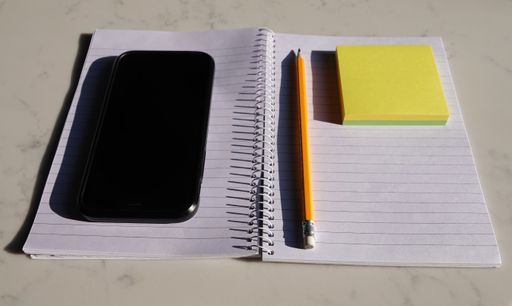 An open notebook with a pencil, a phone and sticky notes on it on a table