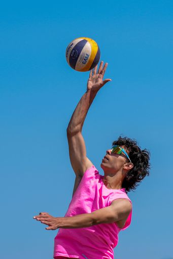 A young man with a bright pink shirt and sunglasses playing volleyball.