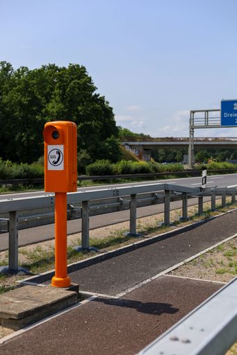 A close-up of a bright orange emergency telephone on the side of an empty highway