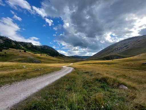 A scenic, winding road leading to a stunning valley, with cloudy skies and lush green grass