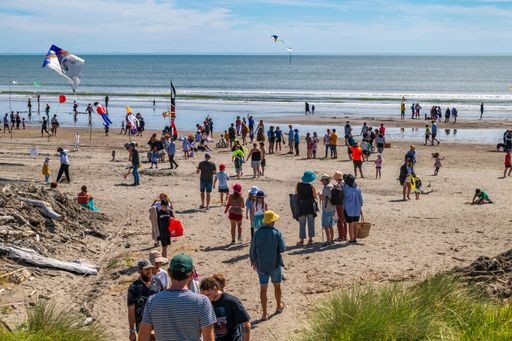 A large group of individuals gathered on the beach, with their backs to the camera, enjoying a sunny day by the sea