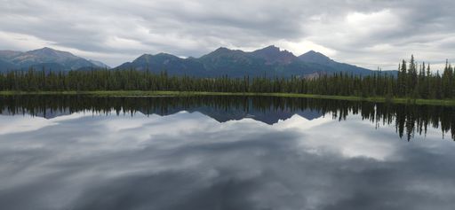 A panoramic view of green trees and mountains reflecting on a tranquil lake on a cloudy day