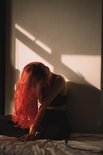 A vertical shot of a lonely woman with red hair sitting in the bedroom