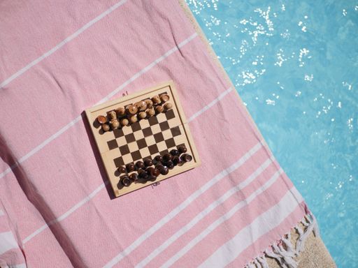 A top view of a chess board on a pink blanket near a swimming pool