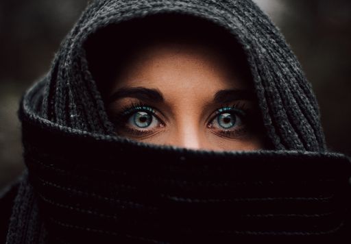 A portrait of a veiled blue-eyed Muslim young girl against a dark blurred background