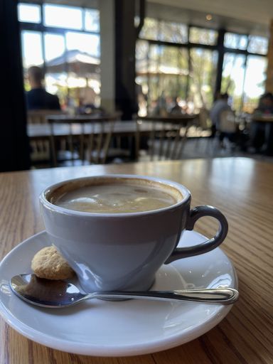 A selective focus shot of a cup of coffee with a spoon and small cookie