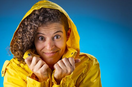 A portrait of a funny adult woman with curly hair wearing a yellow coat against a blue background