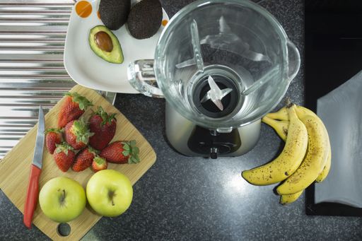 A top view of fresh fruit and a blender on a kitchen marble counter