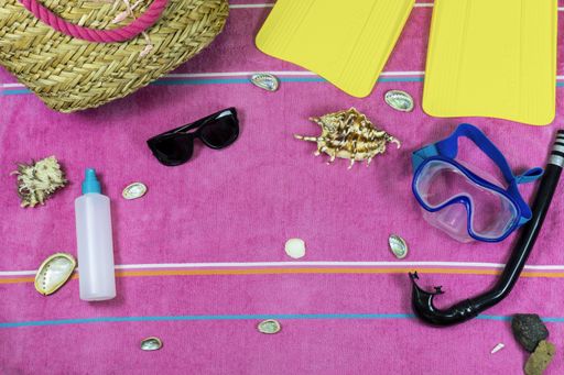 A flat lay of swimming items on a pink background