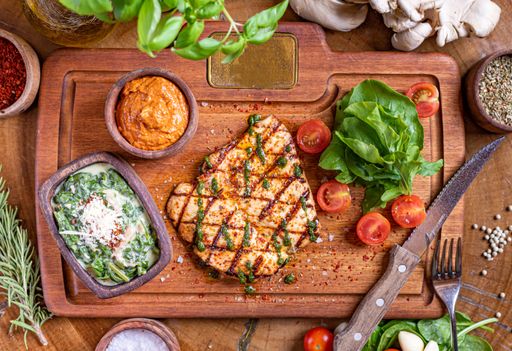 A high-angle shot of a  tasty Grilled Chicken on a wooden cutting board under the natural light