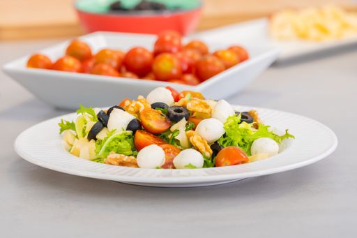 A serving of Mediterranean diet salad Santorini with mozzarella, walnuts, cherry tomato, apple, assorted lettuce, black olives, olive oil