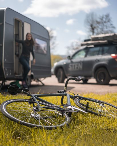 A vertical shot of a caucasian woman near the caravan car and a car, bicycle on the street
