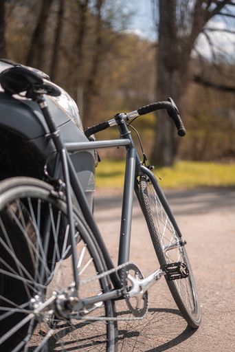 A vertical shot of a black bicycle leans on the car in the street