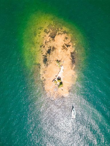 An aerial view of a boat in crystal-clear waters near a picturesque island shore