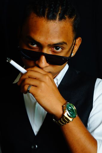 A handsome Indian man in a suit and a silver watch smoking a cigarette looking at the camera