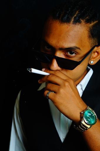 A handsome Indian man in a suit and a silver watch smoking a cigarette looking at the camera