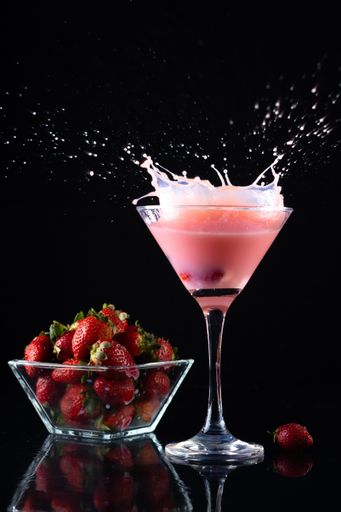 A vertical shot of smoothie in a glass and a small bowl with strawberries on a dark background