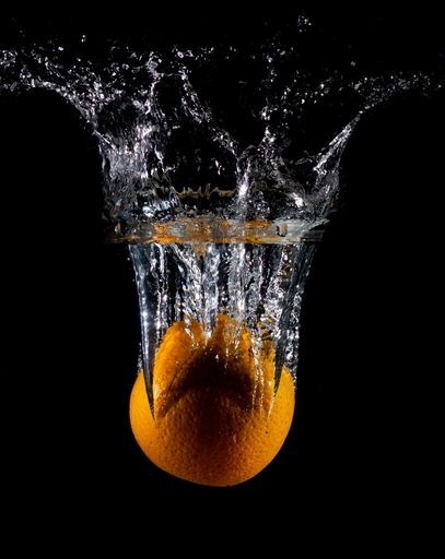 A vertical shot of an orange in water with splashes on a dark isolated background