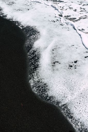 A vertical shot of foamy waves washing the black sand beach