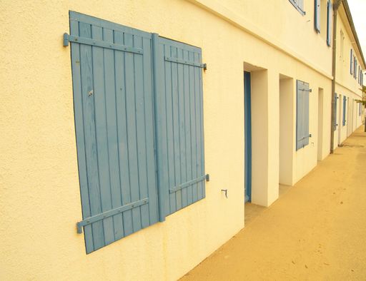 A long shot of a yellow building facade with bluish widows and doors