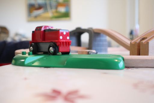 A red toy car on a wooden table under the lights with a blurry background