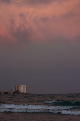 A vertical shot of fiery red sunset seen through sea waters on background of buildings