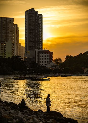 A vertical shot of silhouettes of people on the shore at sunset in Penang, Malaysia