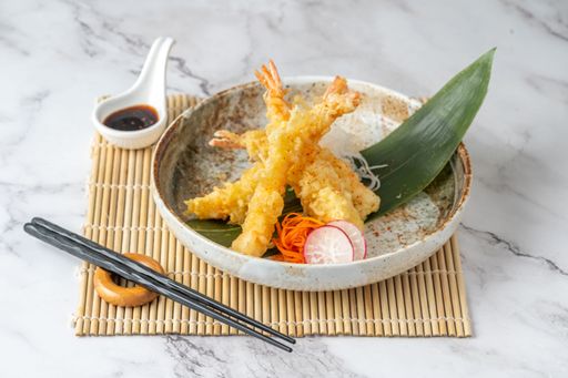 A close-up of a bowl of tempura shrimp with soy sauce and chopsticks next to it