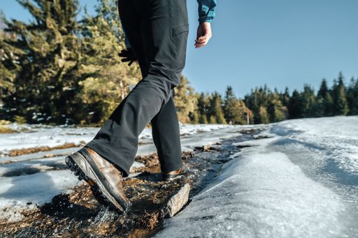 Trekking or hiking on a wet trail. Close up shot of hiking boots or shoes. Outdoor path with snow and water. Detail photo of outdoor hiking boots.