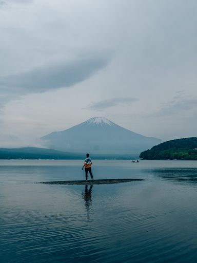 A rear view of a young man standing on the lake with Mount Fuji background in Tokyo, Japan