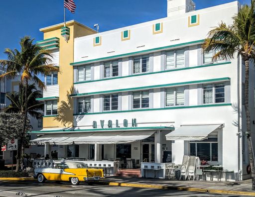 A yellow vintage car parked on the street against Avalon hotel in Miami, Florida