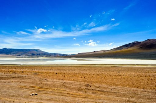 An empty desert landscape around hills with a lake beneath a bright blue sky