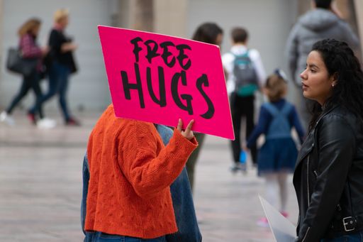 Millennial woman with pink sign offering Free Hugs