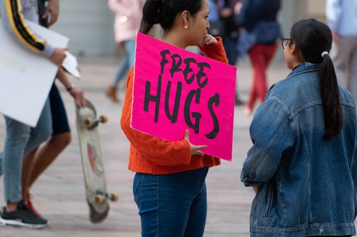 Millennial woman with pink sign offering Free Hugs