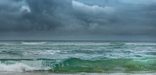 A blue-green wave breaks under stormy skies in South Africa, from Kleinkrantz beach in the Western Cape's Garden Route.