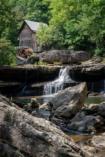 A wooden house with a cascading stream running through a lush green forest in Babcock State Park, West Virginia, USA