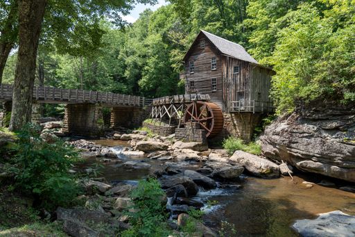 A wooden house with a cascading stream running through a lush green forest in Babcock State Park, West Virginia, USA