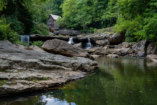A wooden house with a cascading stream running through a lush green forest in Babcock State Park, West Virginia, USA