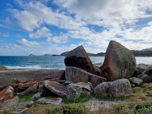 A serene beachscape featuring an abundant array of large rocks and tranquil blue water in the background