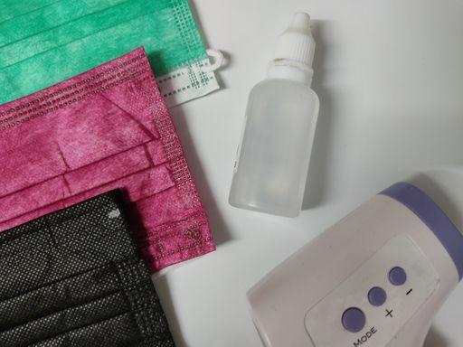An overhead shot of a sanitizer and masks of different color and a temperature meter
