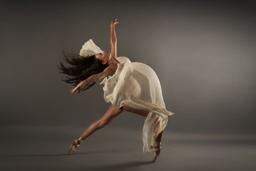 A young Hispanic pregnant ballerina performing classical ballet pose with a silk cloth in studio