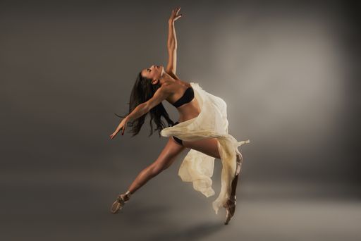 A Hispanic ballet dancer with black lingerie and gauze covering her doing dance pose