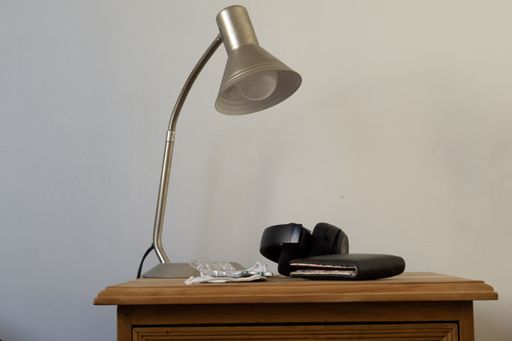 A wallet, face mask, pills, sunglasses and a lamp on a shelf by the bed