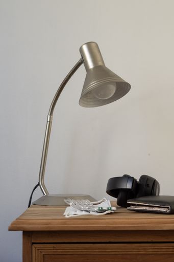 A wallet, face mask, pills, sunglasses and a lamp on a shelf by the bed