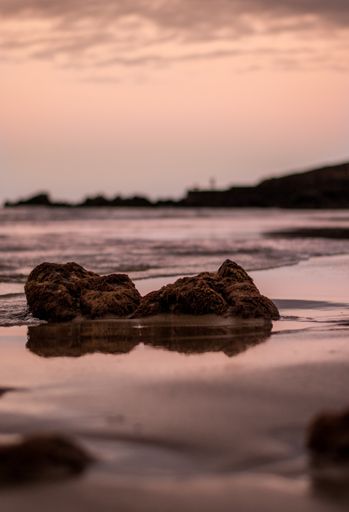 A vertical shot of rocks at shore reflecting on wet sand