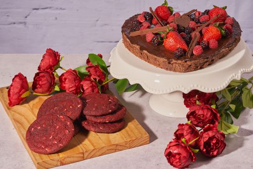 A closeup of a heart-shaped brownie cake and red velvet cookies with roses to celebrate mother's day