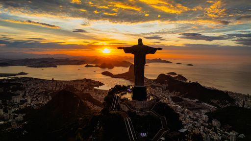 An aerial view of a golden sunset illuminating the statue of Jesus Christ in Rio de Janeiro, Brazil.
