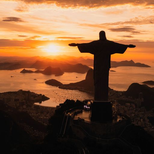 An aerial view of a golden sunset illuminating the statue of Jesus Christ in Rio de Janeiro, Brazil.