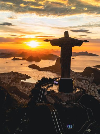 An aerial view of a golden sunset illuminating the statue of Jesus Christ in Rio de Janeiro, Brazil.