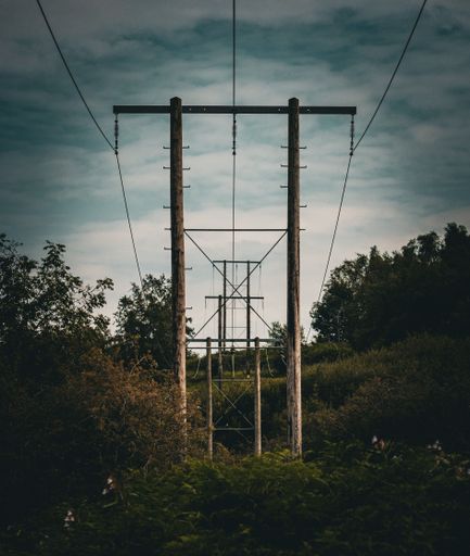 A powerline spanning across a scenic landscape with a backdrop of dark, looming clouds.